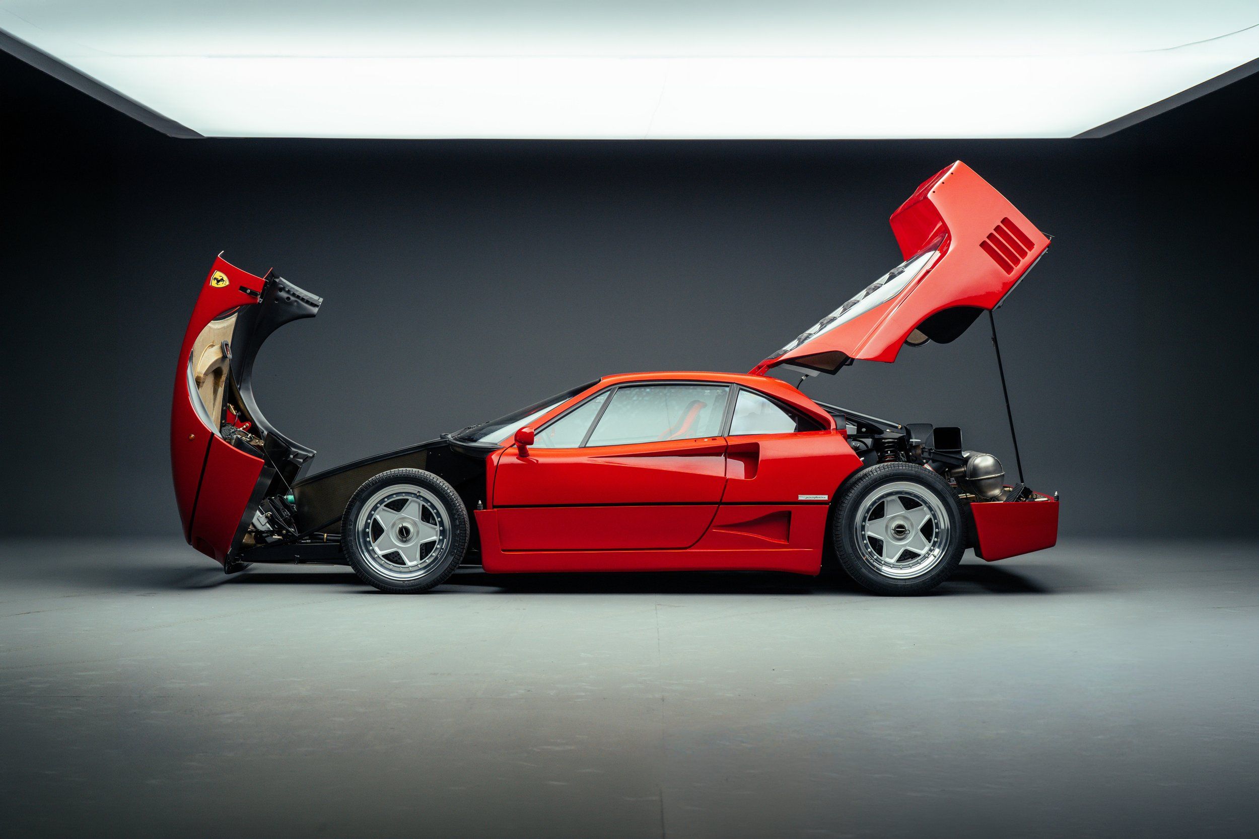 Ferrari F40 1989, side view, rosso corsa, front and rear clamshell panels open revealing engine and mechanics, studio photography. RM Sotheby's auction photography.