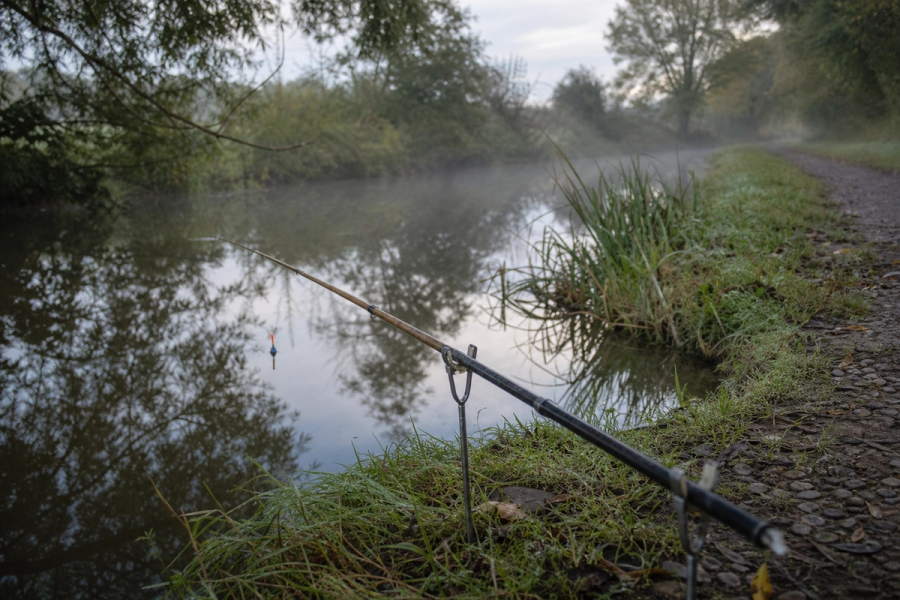 A float rod resting on rod rests beside a still, narrow canal
