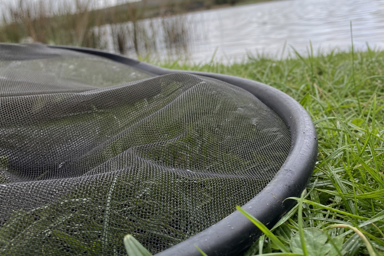 Close-up of fine, soft knotless micromesh in a landing net head, lying on the grass beside a lake