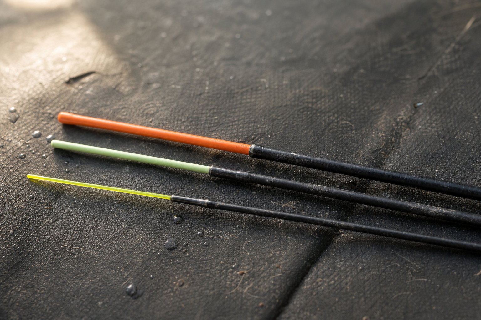 Three quivertips of different stiffness laid side by side on a dark tackle mat