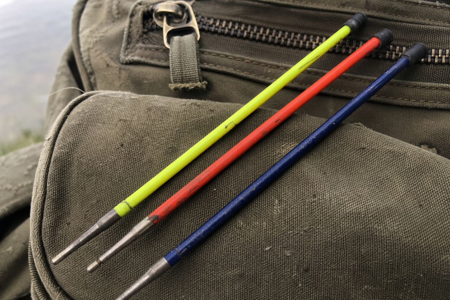 Three interchangeable quivertips of different colours laid side by side on a fishing bag