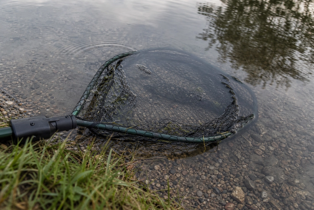 Knotless landing net fully submerged in calm still water at a fishery bank