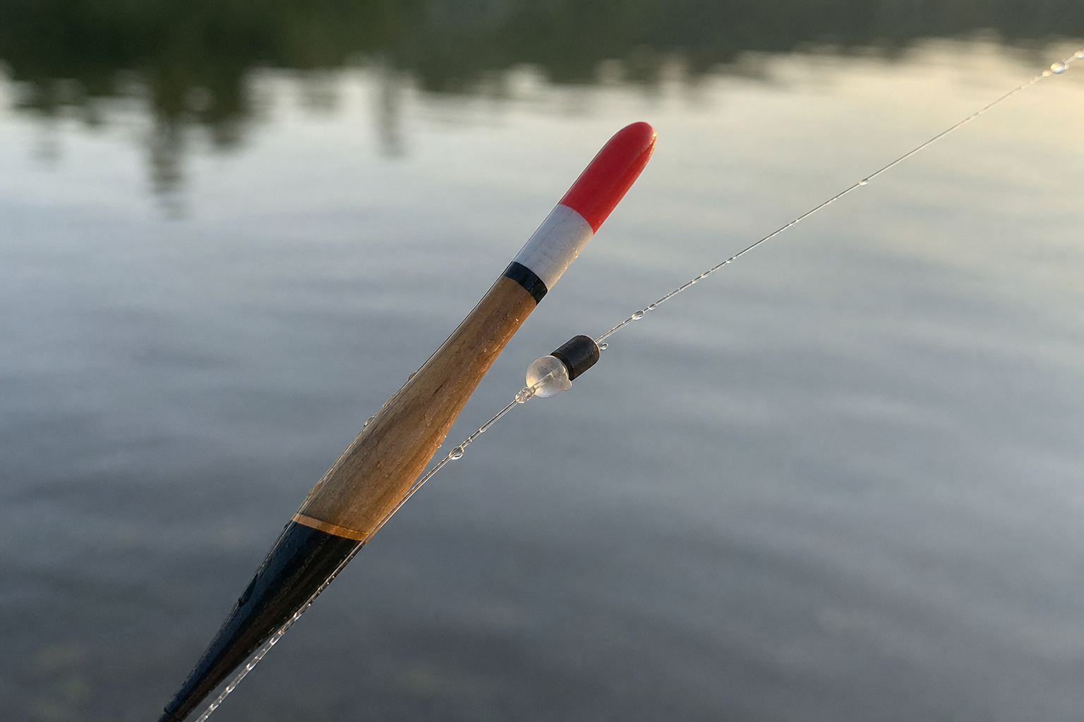 Close-up of a float stop and waggler float on fishing line against blurred water background