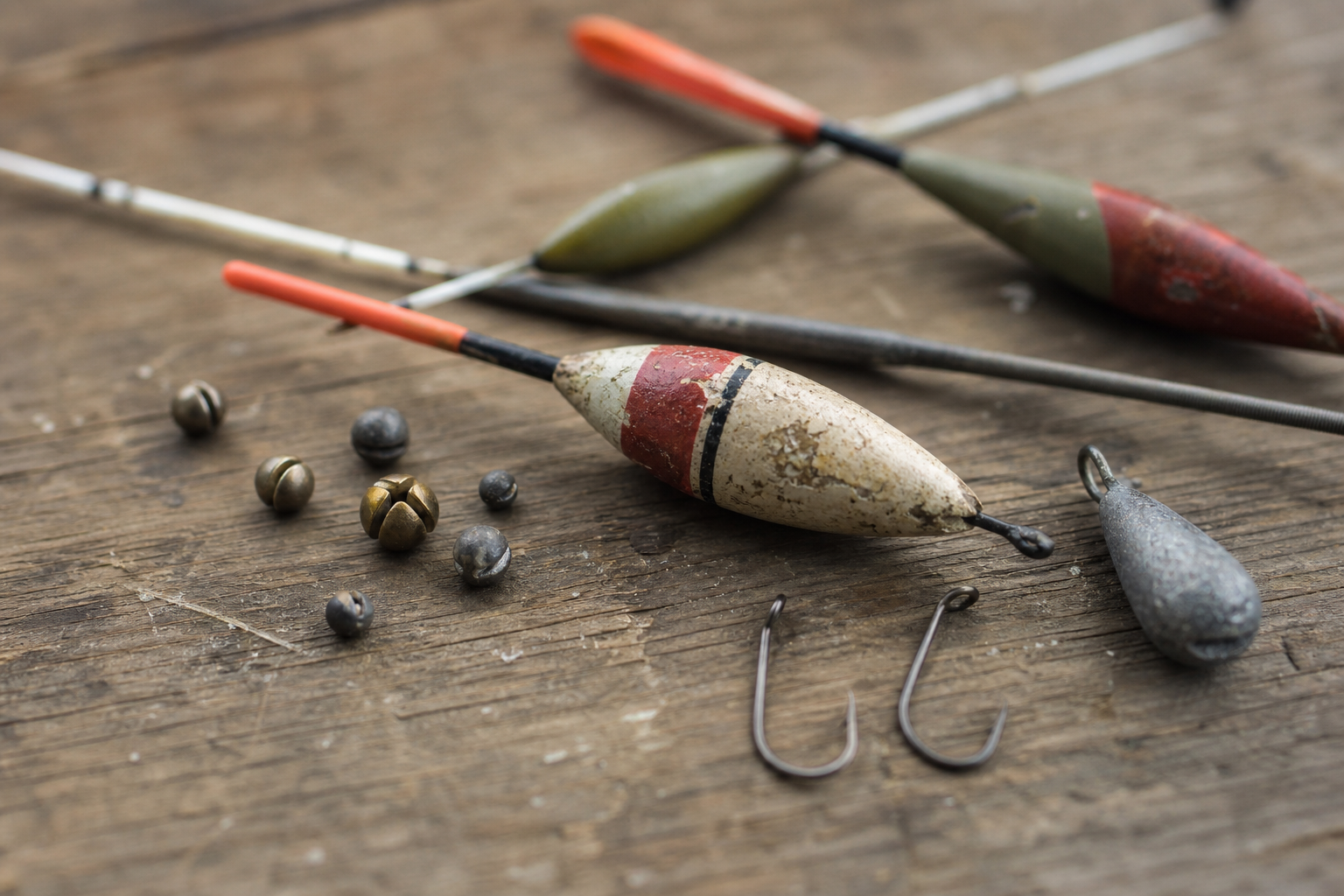 A selection of floats, split shot, barbless hooks and a plummet on a wooden surface