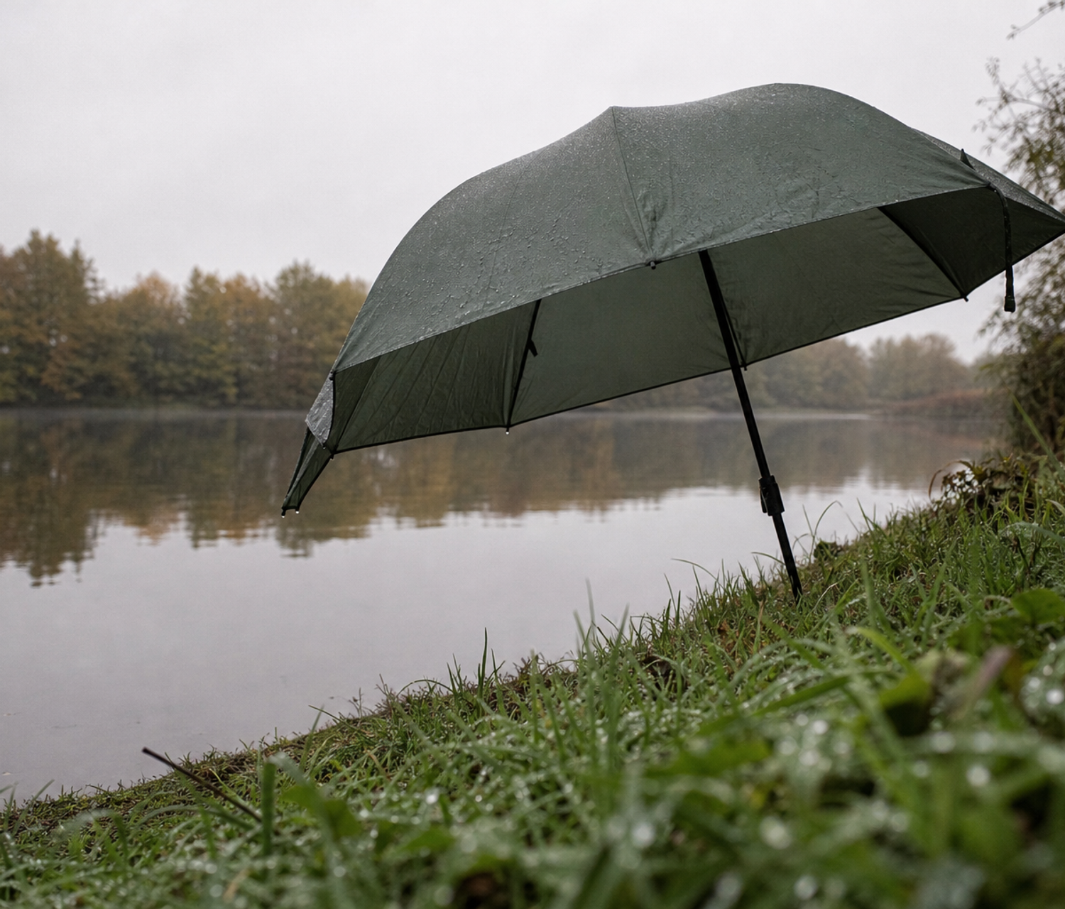 Green fishing umbrella pitched on a grassy stillwater bank in overcast light