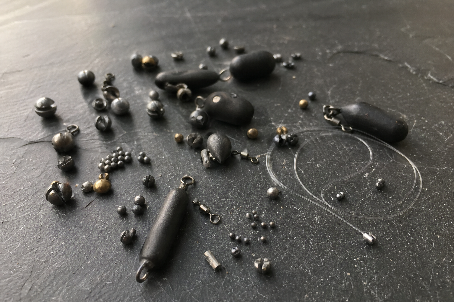 Assorted non-lead fishing shot and leger weights arranged on a dark surface