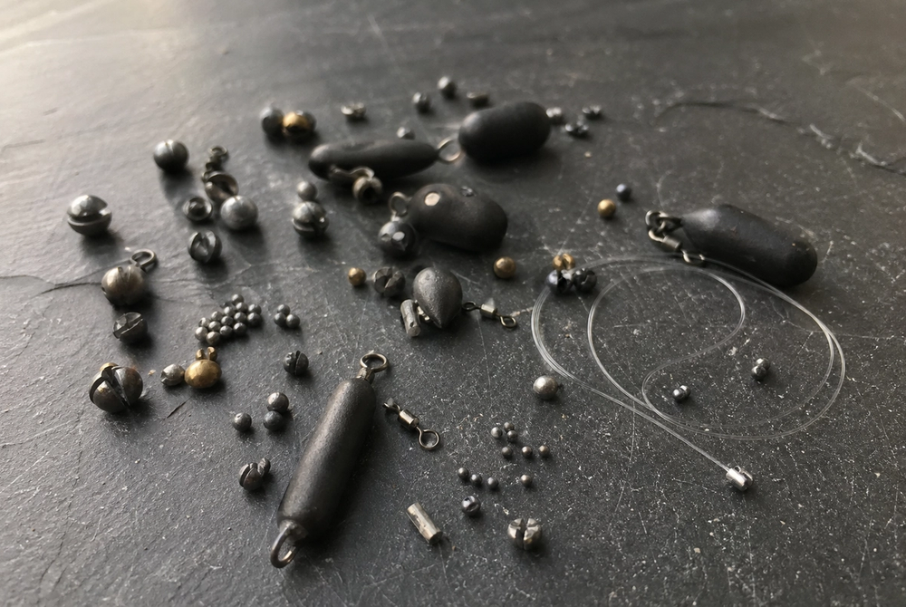 Assorted non-lead fishing shot and leger weights arranged on a dark surface