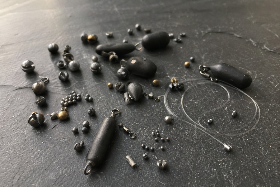 Assorted non-lead fishing shot and leger weights arranged on a dark surface