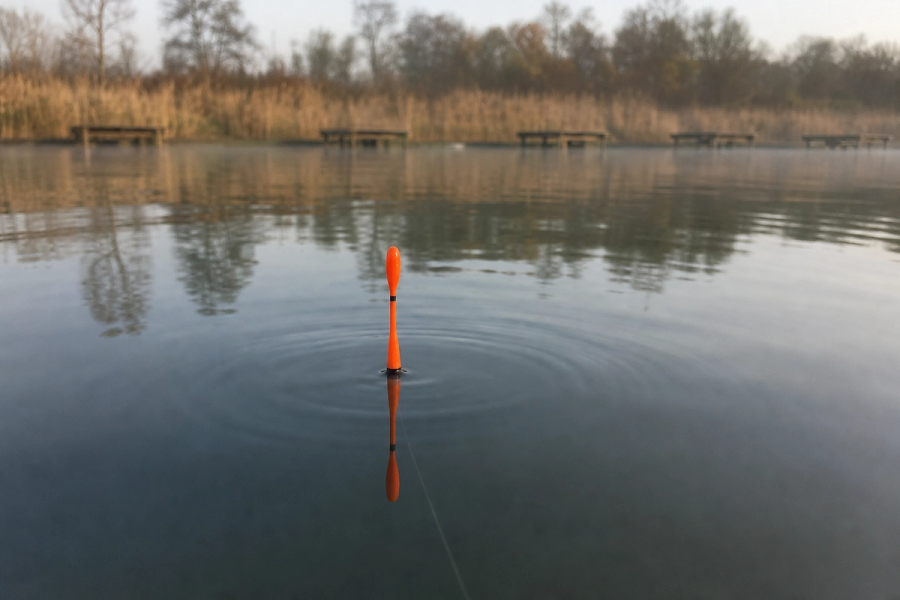 Bright orange waggler float sitting upright on calm lake surface at a commercial fishery