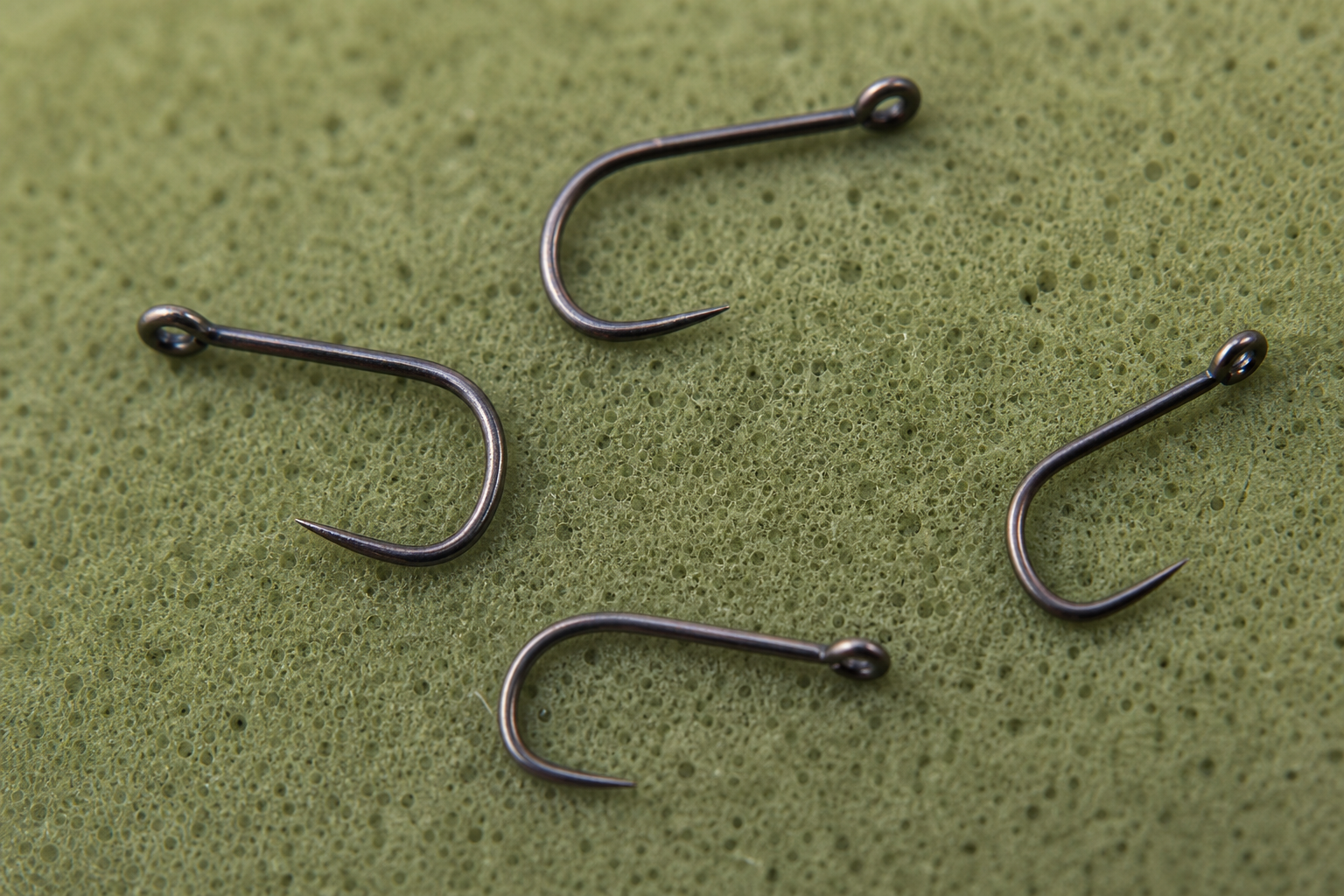 Four small barbless coarse fishing hooks lying on a green unhooking mat