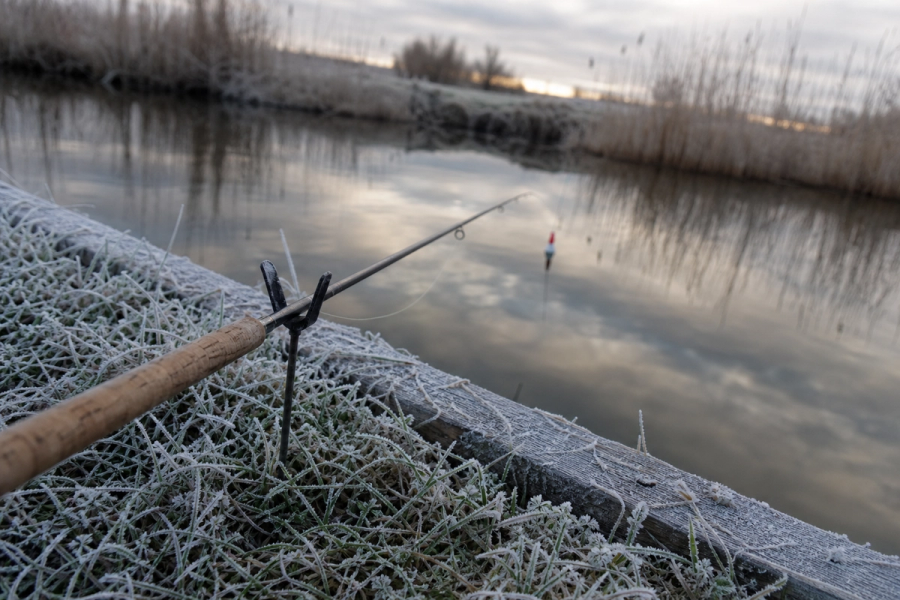 Frost-edged canal bank with float fishing rod resting on rod rest