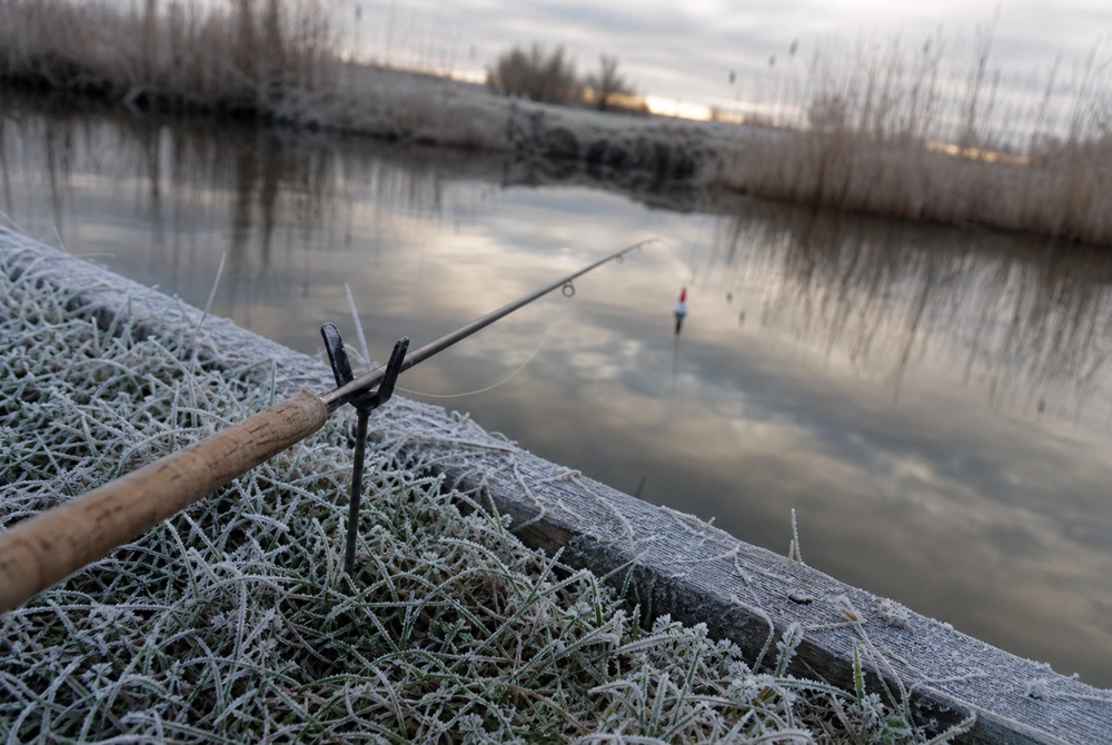 Frost-edged canal bank with float fishing rod resting on rod rest