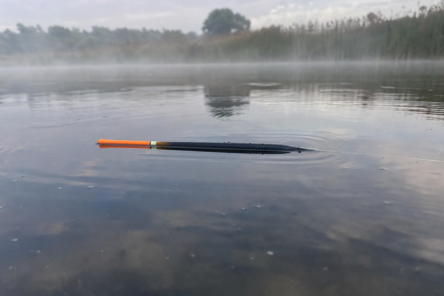 A waggler float lying horizontally flat on the surface of a still lake during a lift bite