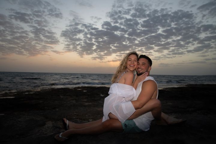 Couple cuddling on the beach beneath a dramatic sunset sky in Cyprus
