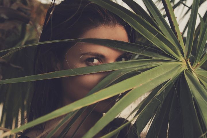 Artistic outdoor portrait of a woman peeking through tropical palm leaves in Cyprus