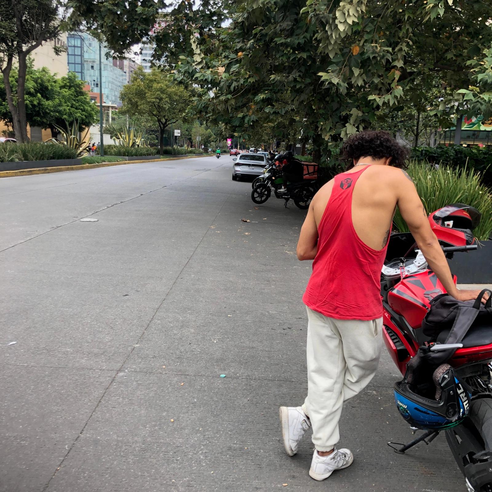 Al oeste de la Ciudad de México, un repartidor espera junto a su motocicleta que su celular reciba una orden para entregar comida, una escena común afuera de los centros comerciales de México. Foto: @EduPortas