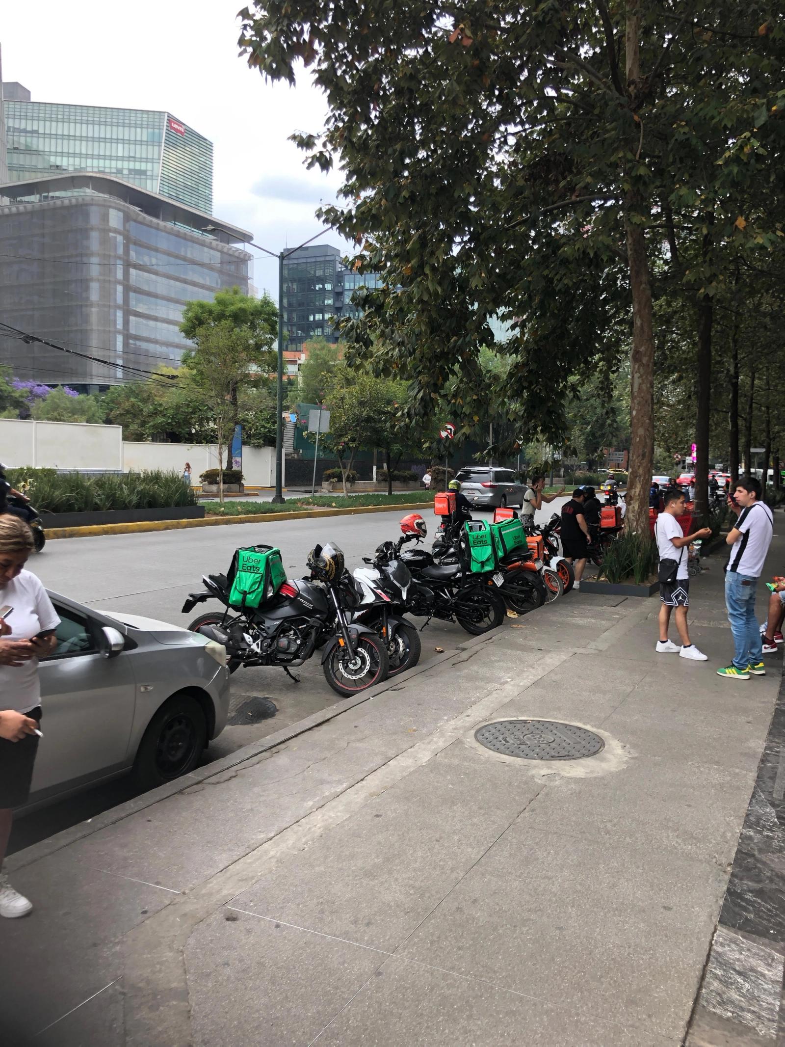 Un grupo de repartidores aguarda en sus motos para entregar la orden que recibirán mediante una app en su teléfono. Foto: @EduPortas