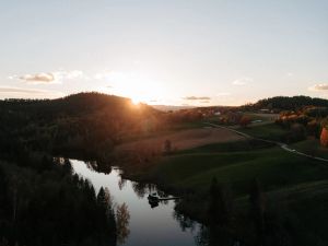 Dronebilde over kulturlandskap i Telemark, med flytende badstueflåte i solnedgang