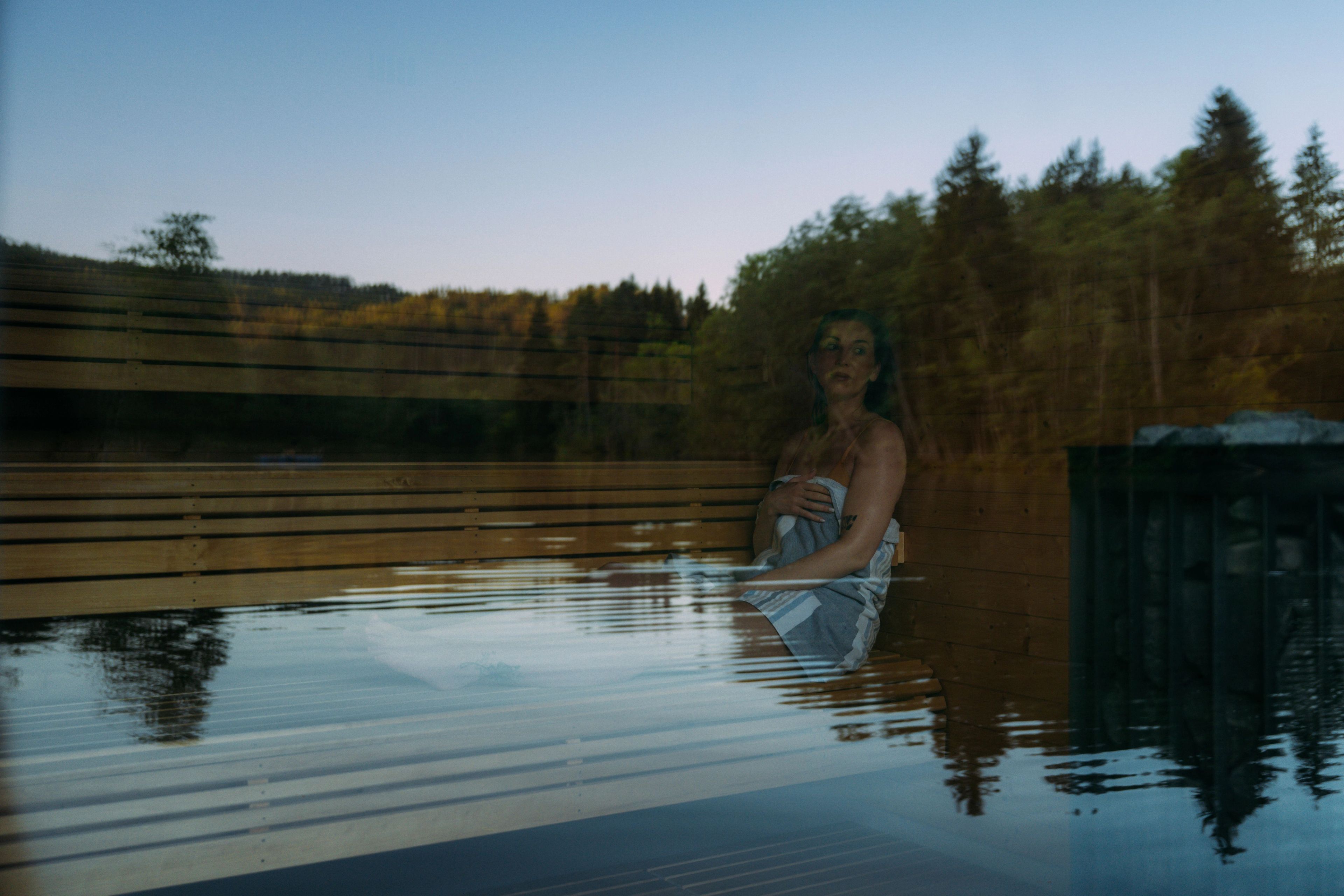 Dame sittende på badstubenk med refleksjoner av vann i vinduet