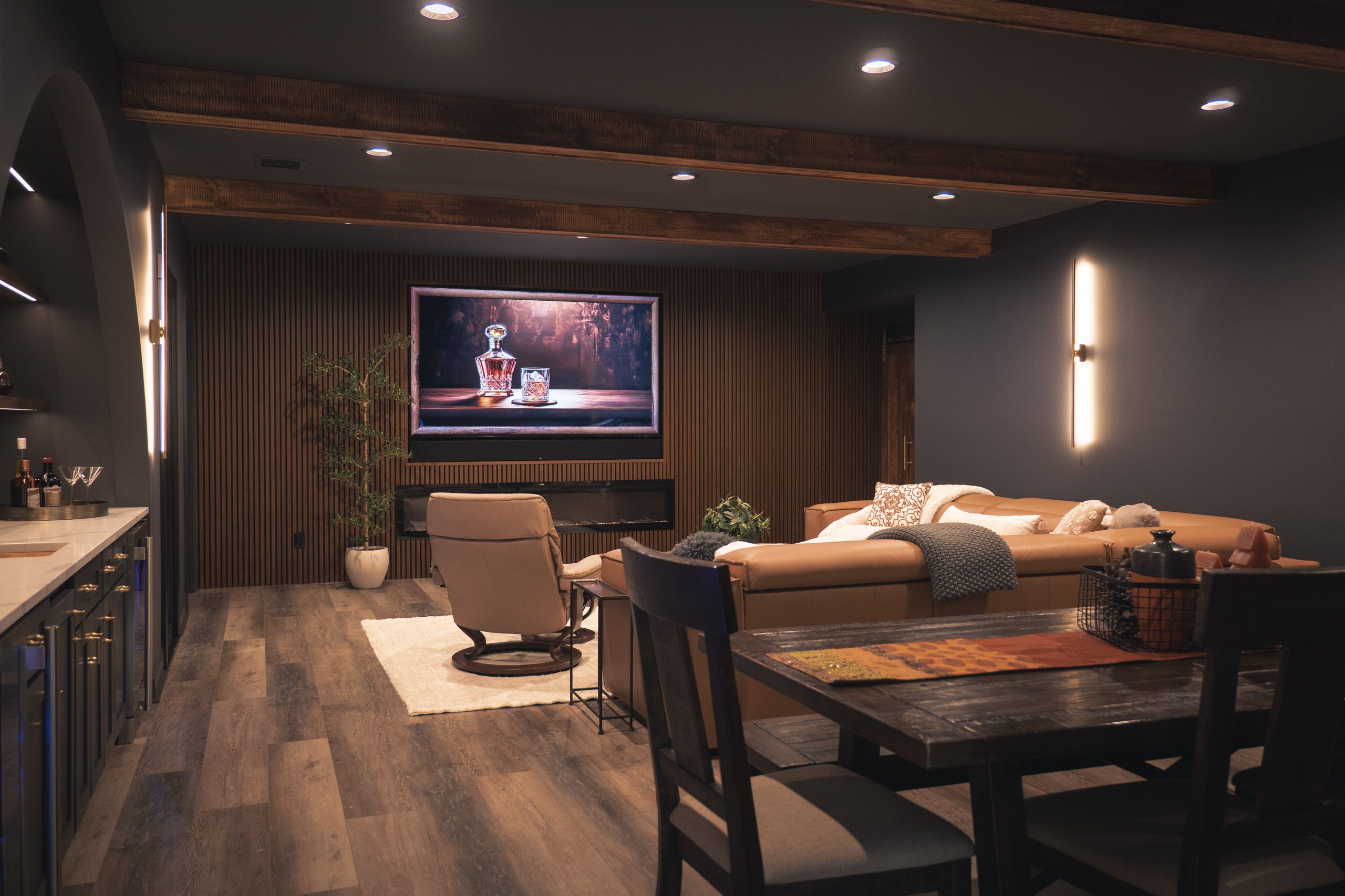 Dark, moody basement with faux wood beams and fluted panel entertainment wall 