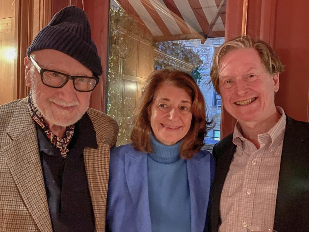 A photo of three people smiling at the camera. On the left, Frederic wears a navy beanie, a dark pair of glasses, and a plaid brown jacket. Karen, center, wears a blue turtleneck and blue blazer. Thomas, on the right, wears a black blazer and a plaid button-down shirt.