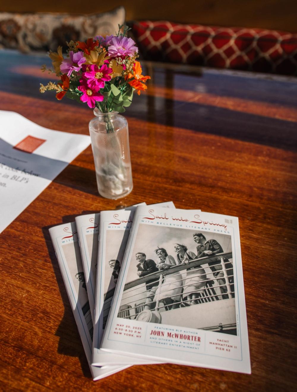 photograph of fête brochures on a wooden table with a vase of pink flowers