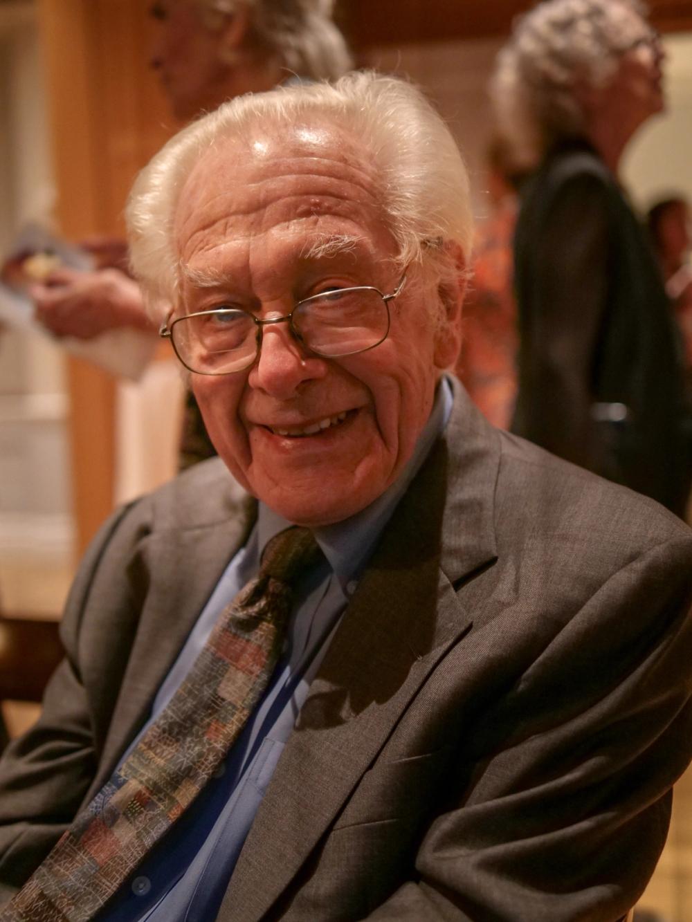 A photo of a man smiling at the camera. Jerry is wearing a dark grey suit and a multicolored tie.