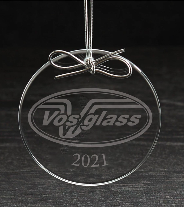 Clear round glass ornament etched with a company logo and the year, tied with a silver cord bow, photographed on a dark wood surface