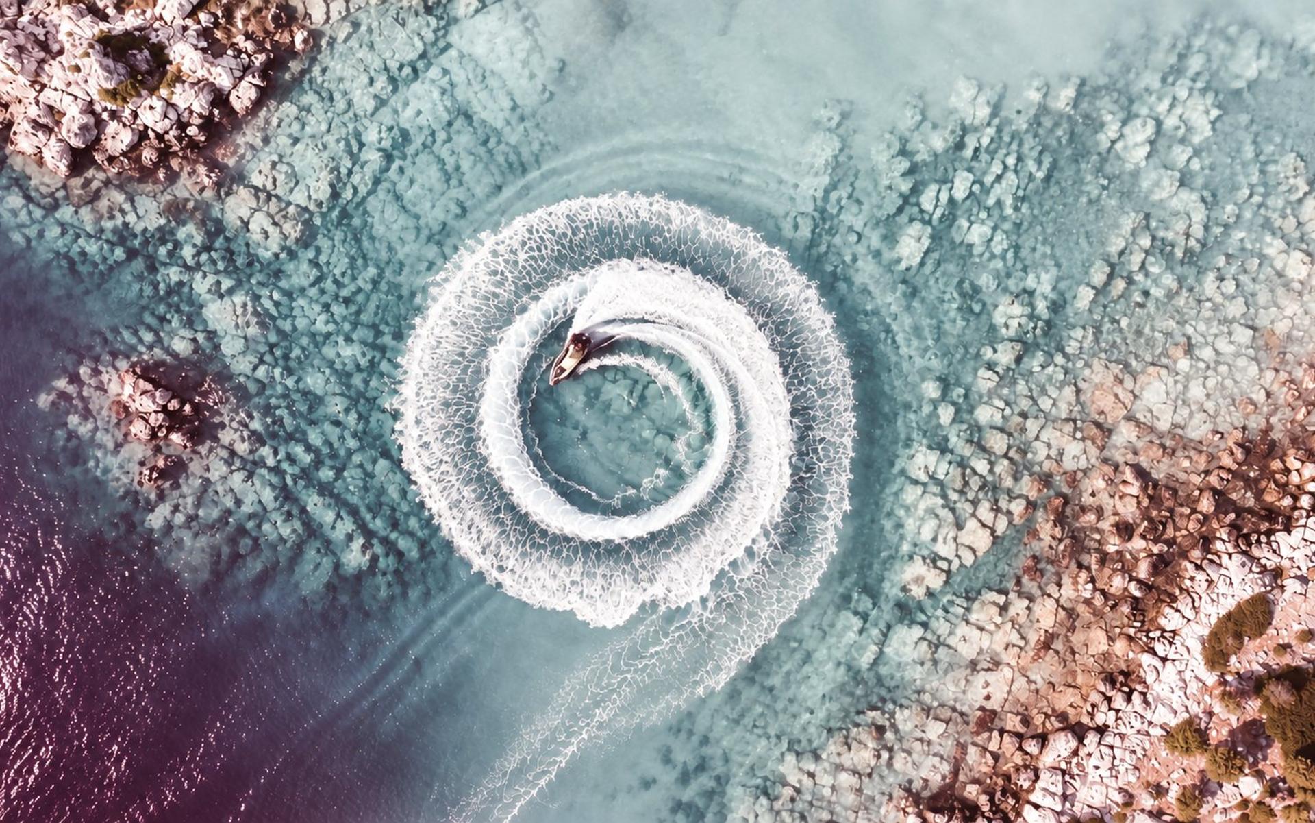 An aerial view of a jet ski carving a spiral wake through turquoise water