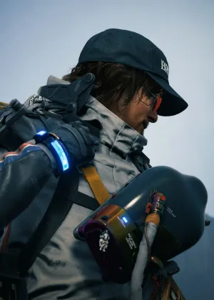 A portrait of Sam in a white Porter suit against an empty pale sky with his face turned away from the camera. He’s holding the strap of his backpack with one hand and wearing a navy blue Bridges cap and red-lensed mirrored sunglasses.