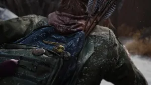 A close up of Ellie’s backpack, adorned with various buttons. There are three arrows sticking out like a makeshift quiver, and the backpack and her jacket have a dusting of snow.