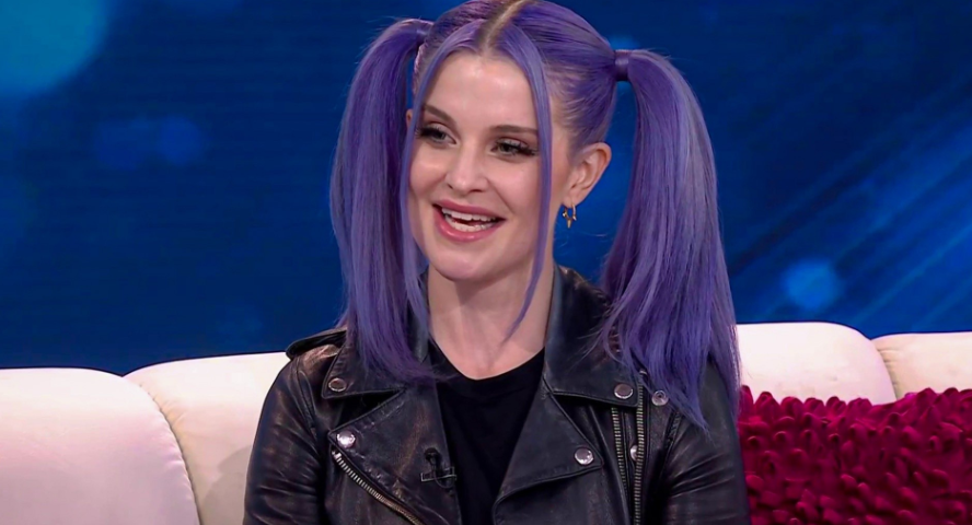 Portrait of Kelly Osbourne showcasing her signature vibrant hairstyle and fashion style while discussing her career milestones and age.