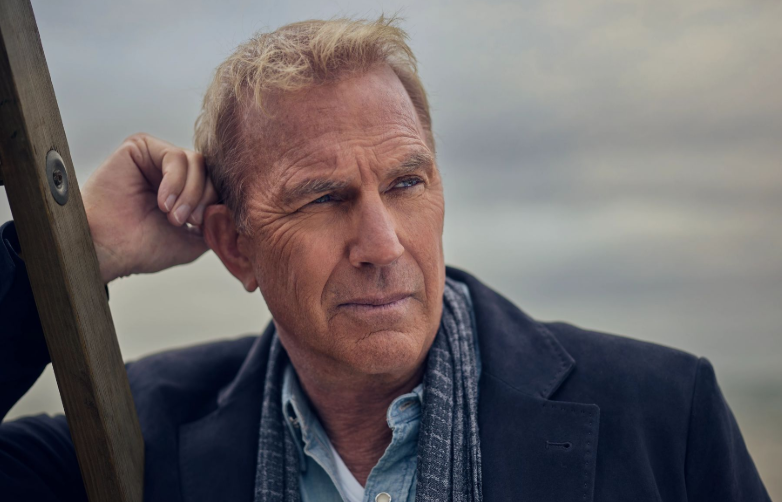 A young Kevin Costner smiling on a classic Hollywood movie set, showcasing his early career charm.