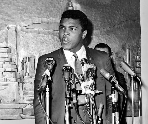 A smiling young Muhammad Ali raises his hands in victory after winning a classic heavyweight boxing match.