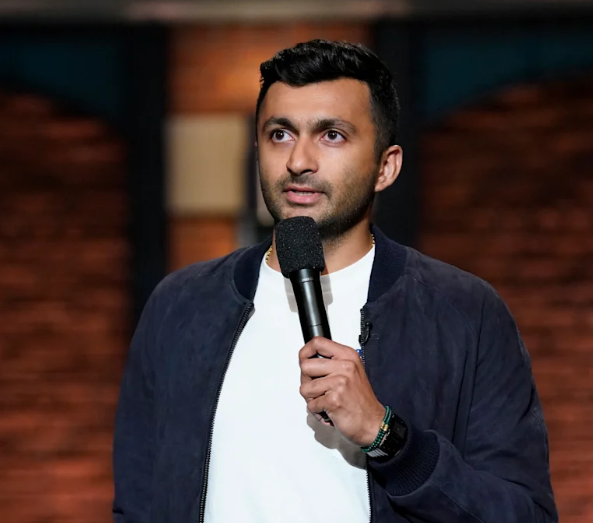 Stand-up comedian Nimesh Patel smiling on stage holding a microphone during a live theater performance