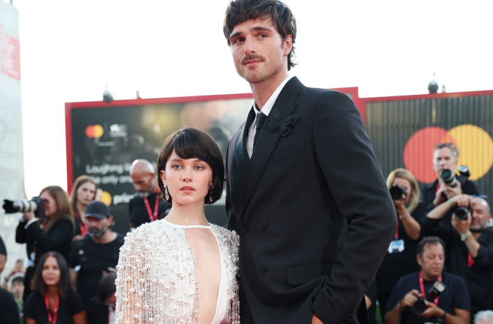 Jacob Elordi smiling on a red carpet while showing off his impressive 6 feet 5 inches height.