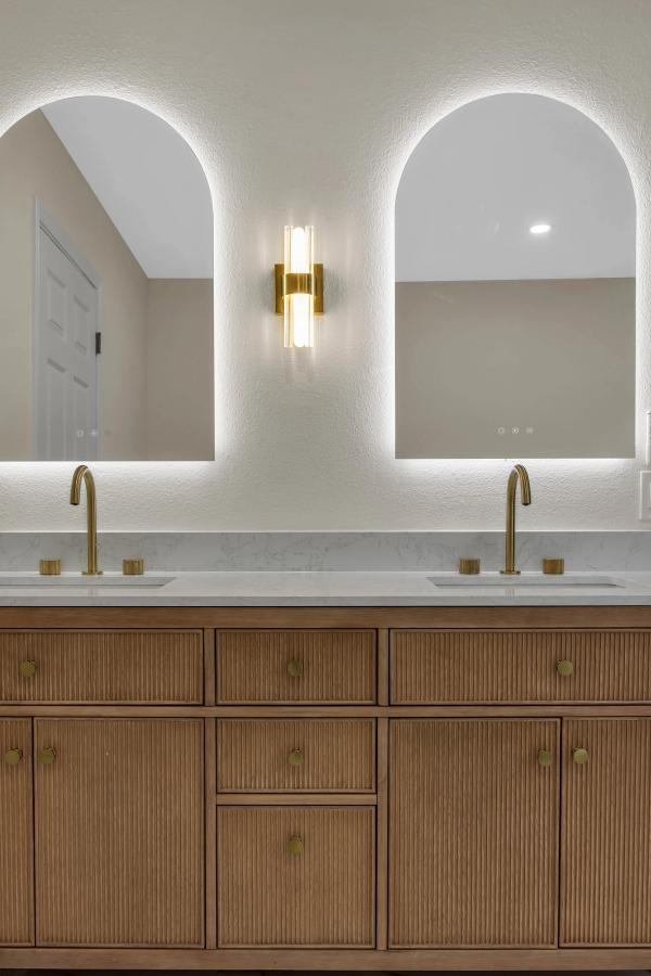 Fluted oak double vanity with dual arched LED mirrors, crystal sconce, and brushed gold faucets