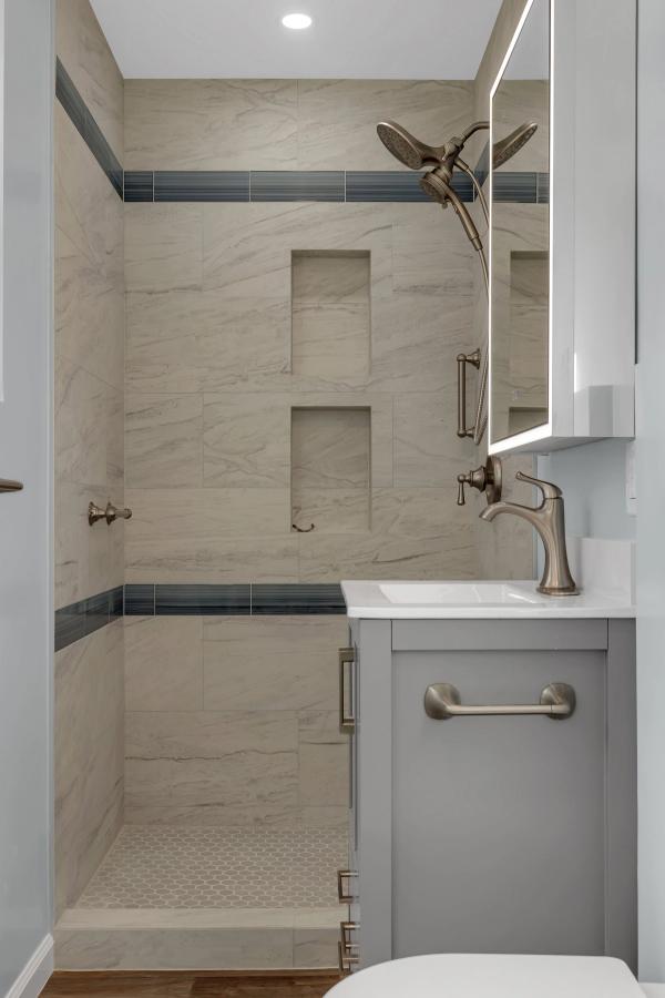 Bathroom, shower and vanity closeup with marble tile, dual niches, and blue accent stripe