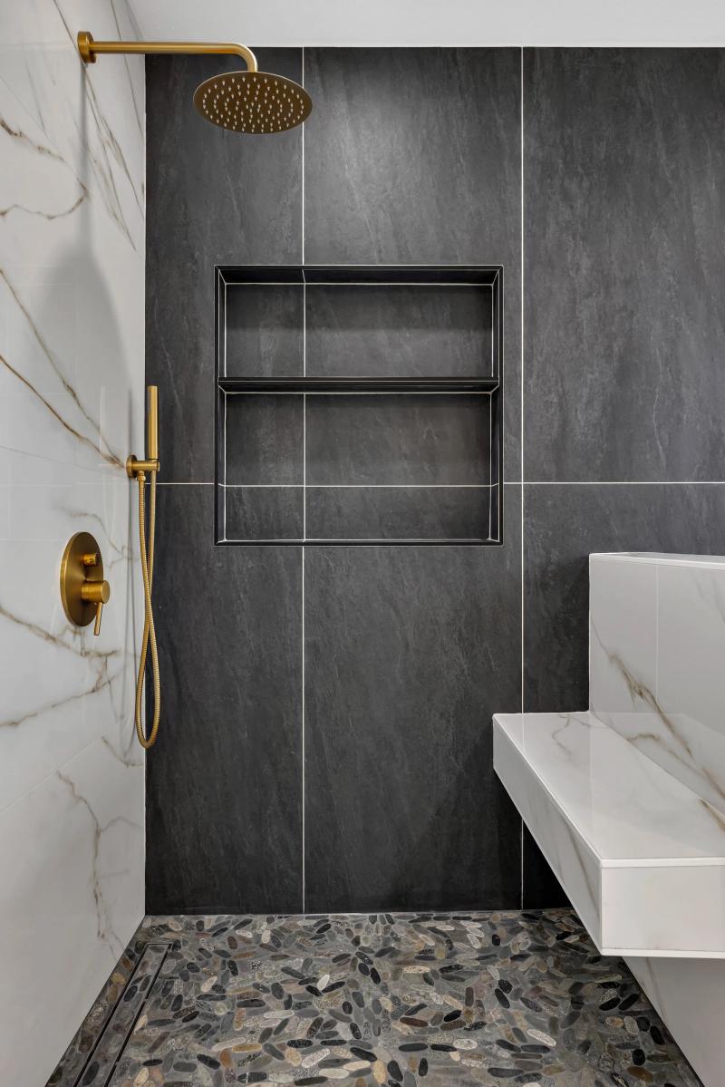 Walk-in shower with dark slate tile, gold rainfall showerhead, and pebble floor — Redwood City bathroom remodel