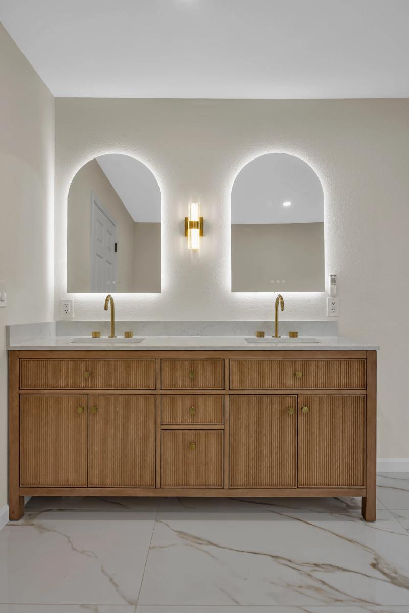 Fluted oak double vanity with arched LED-backlit mirrors and gold gooseneck faucets — Bark and Build Builders