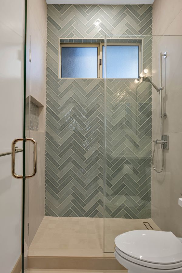 Guest bathroom, sage herringbone tile walk-in shower with glass door and brass handle
