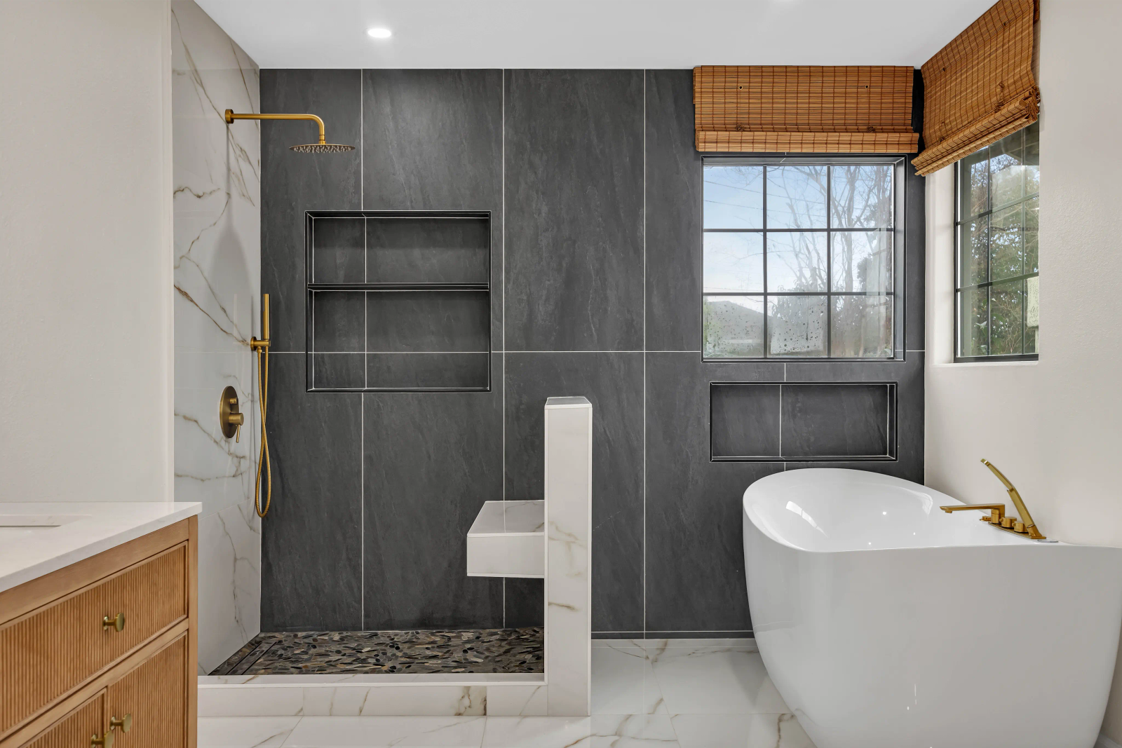 Completed luxury bathroom — dark slate tile shower with gold rainfall fixtures, pebble floor, freestanding soaking tub by Bark and Build Builders