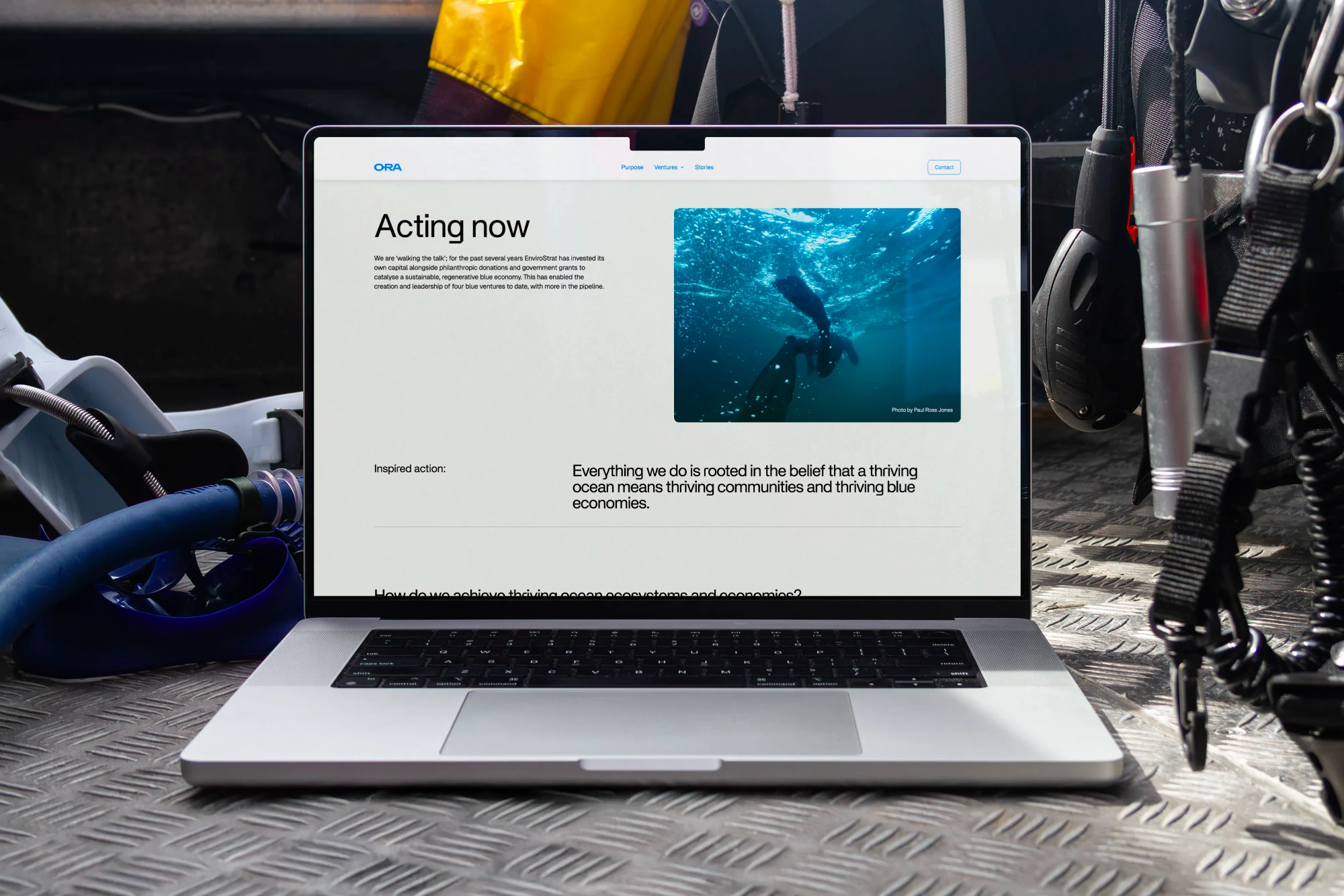 An ORA website page is displayed on a laptop on the metal floor of the diving boat
