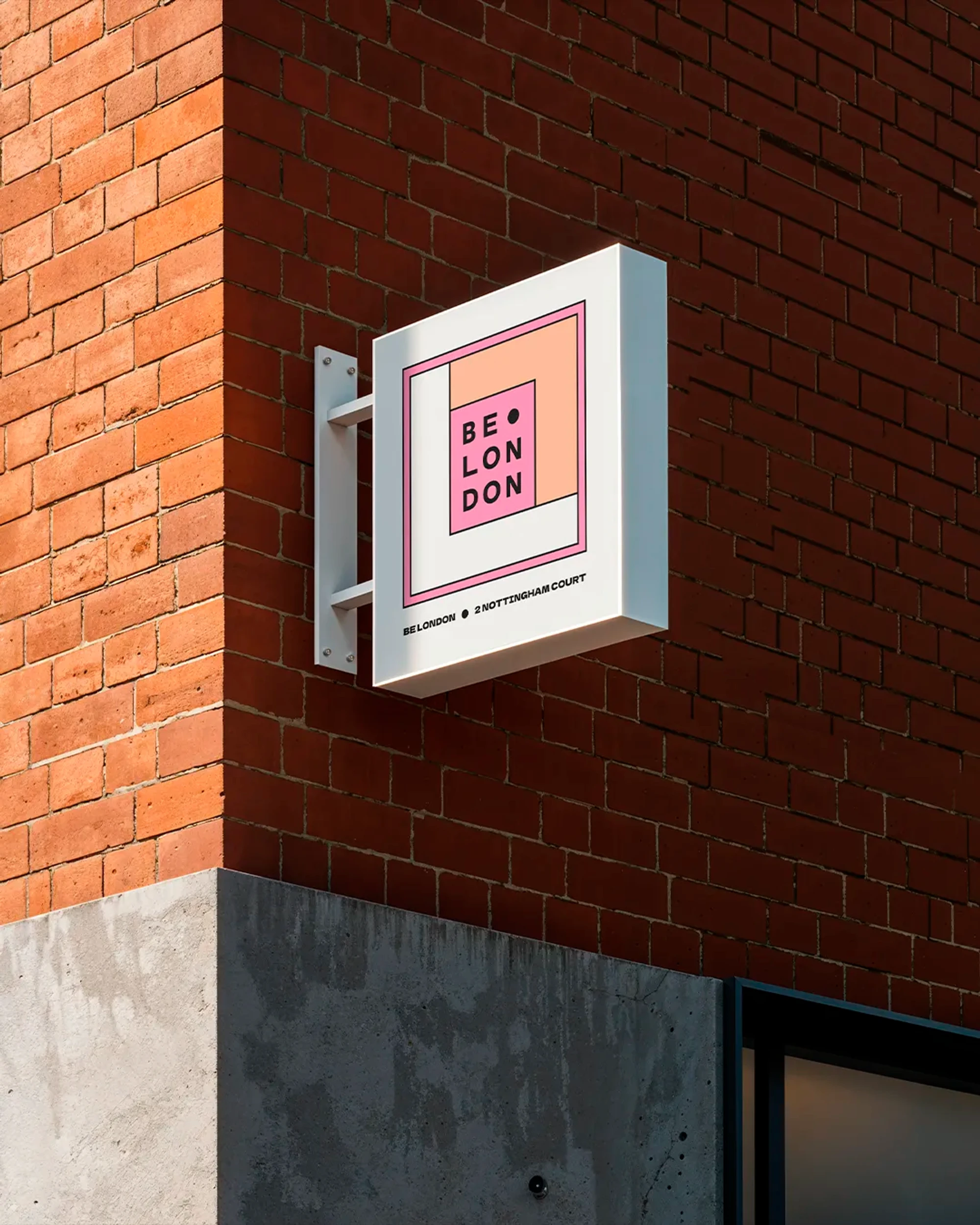 Be London's colourful shop sign hangs on the side of a red brick building.