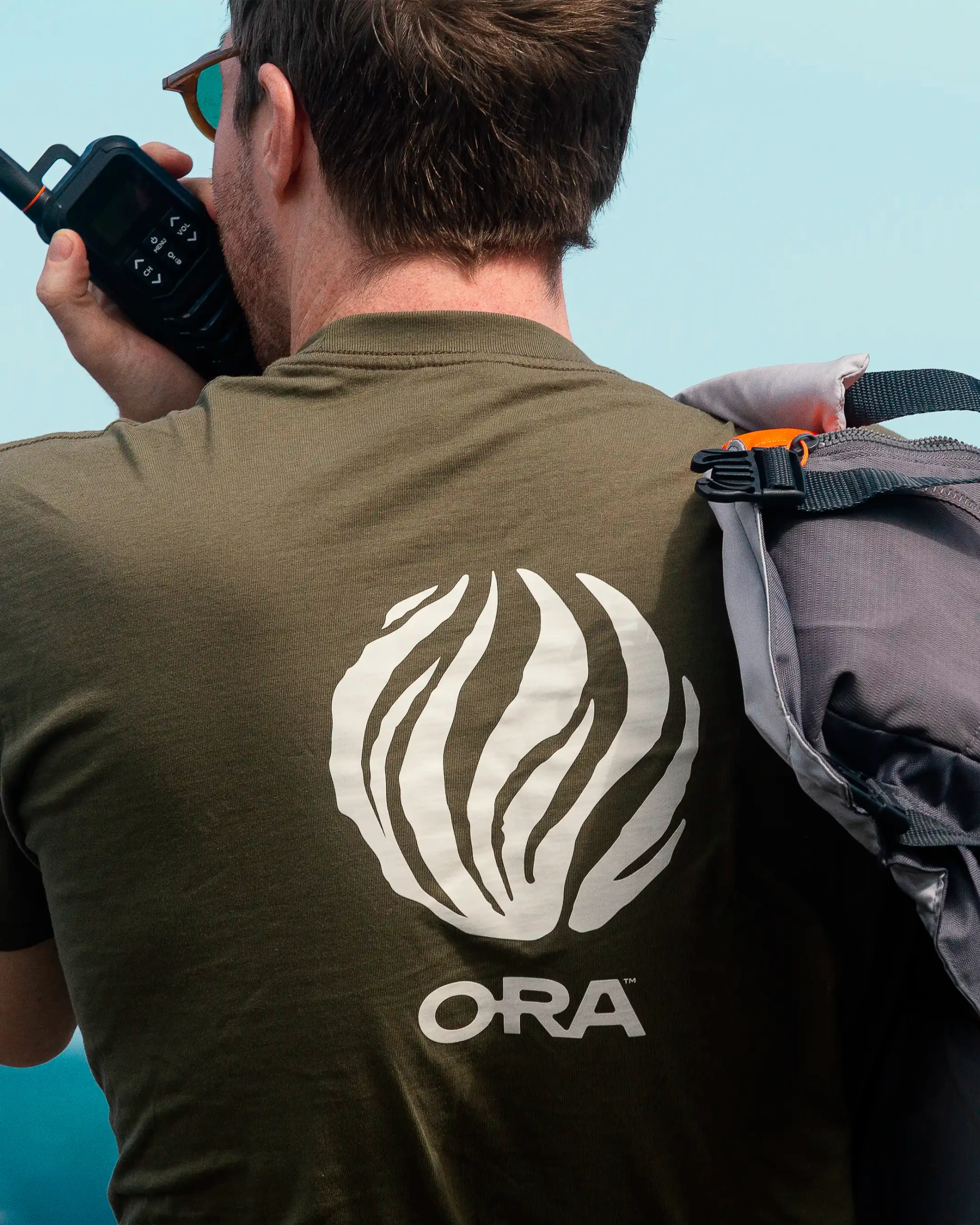 A rear view of a staffer wearing a branded green t-shirt, talking into a radio at sea.