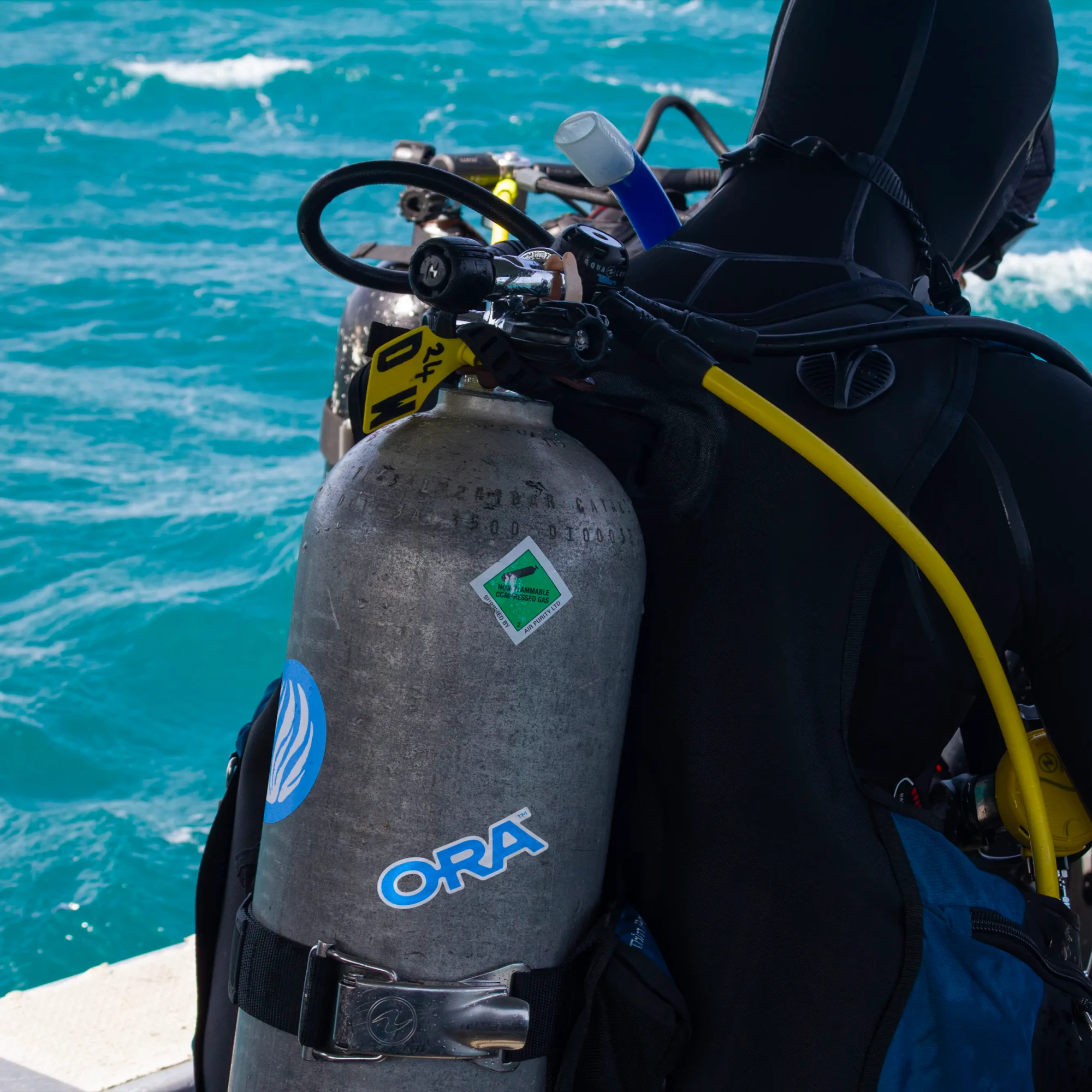 A scuba diver wears an air tank with ORA stickers applied