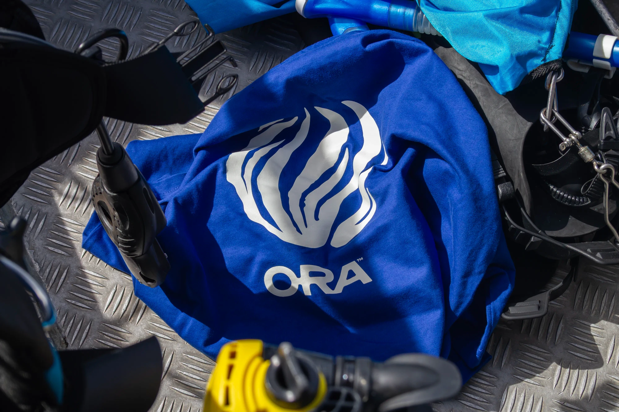 An ORA t-shirt sits crumpled amongst scuba diving equipment on a boat