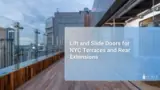 Urban rooftop terrace with wooden decking and glass railings overlooking city high-rises, with large glass sliding doors opening from an interior dining area onto the terrace at dusk