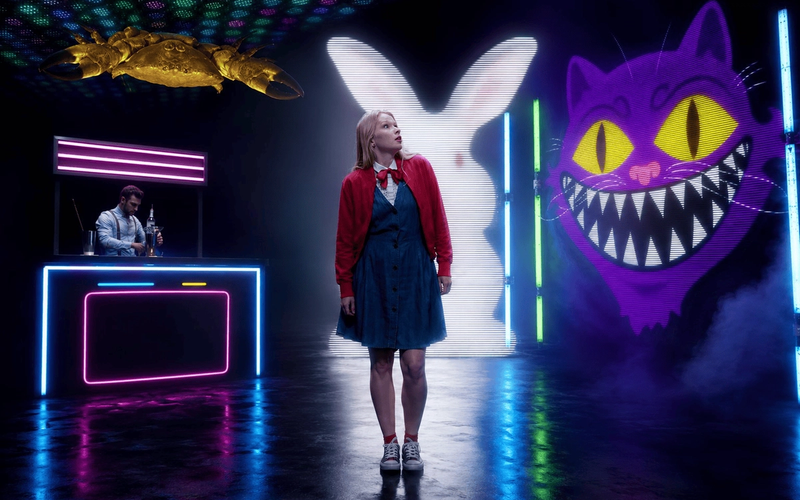 A performer on a neon-lit set with oversized cartoon characters
