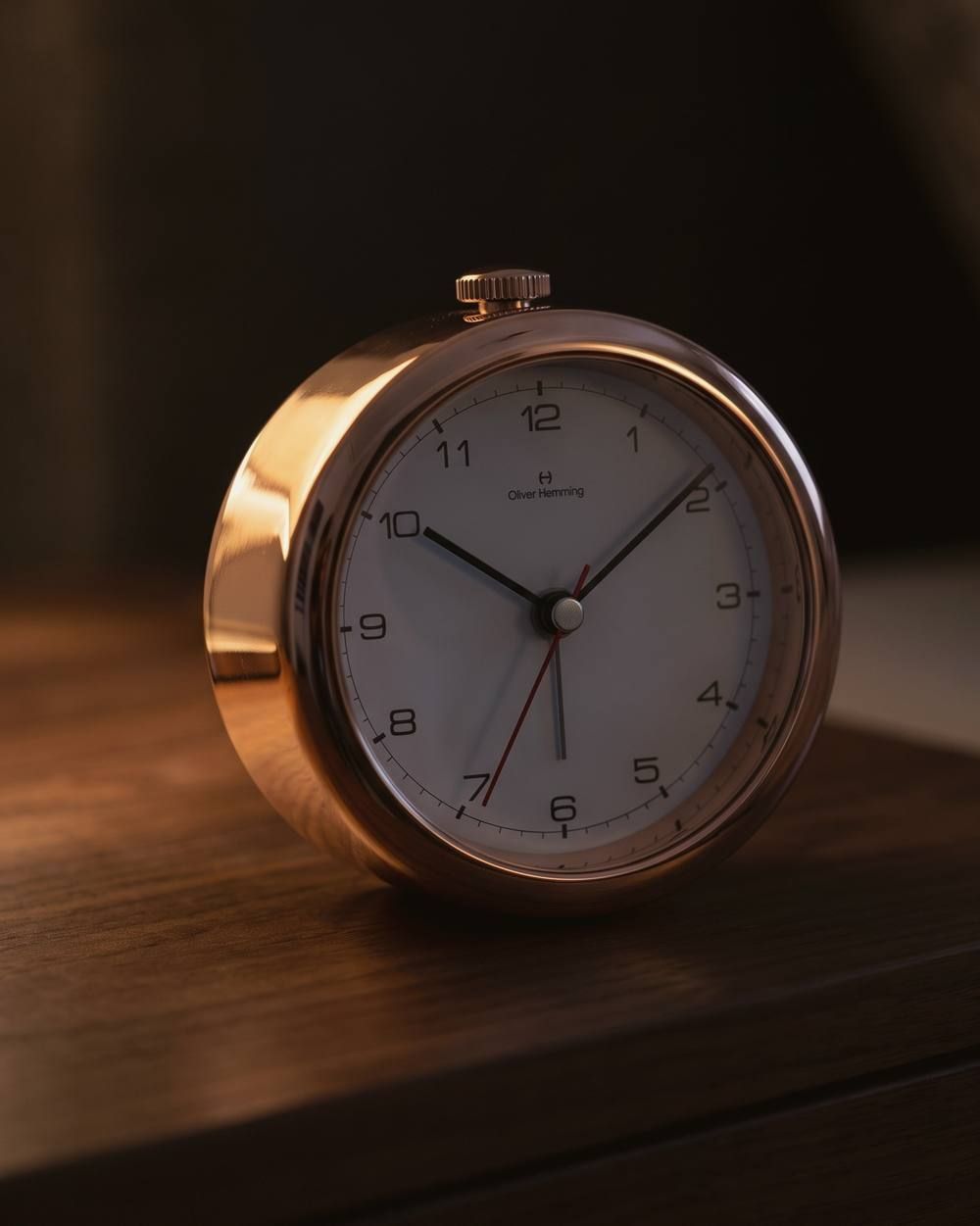 An Oliver Hemming Desire clock in rose gold on a nightstand under lamplight